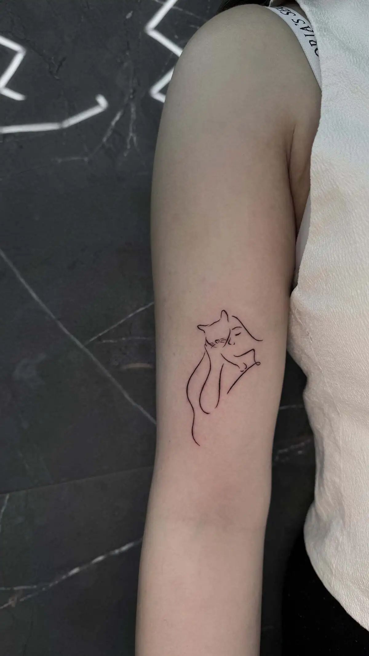 minimal hugging cat woman line arm tattoo